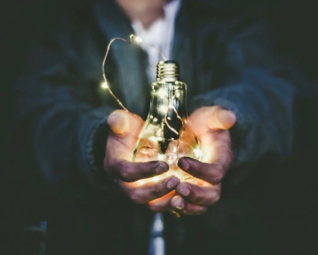 Person holding a glowing light bulb with fairy lights inside, symbolizing creativity, innovation, and new ideas.